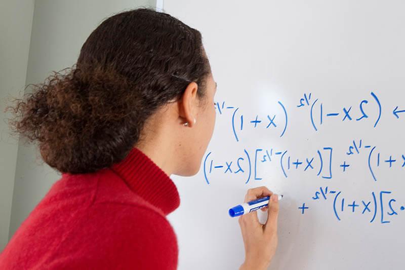 woman writing equation on whiteboard 